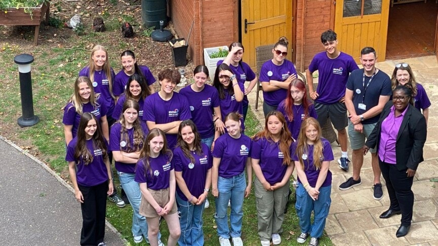 group shot of students in purple polo shirts standing in the care home garden smiling