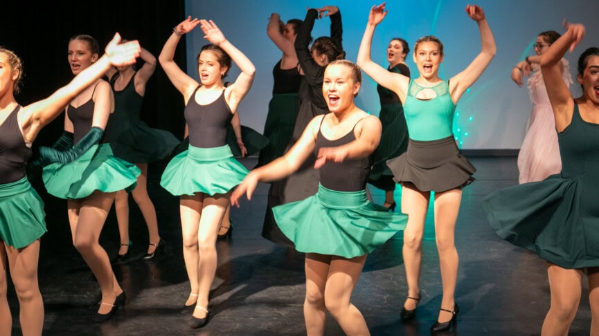 Group of students singing and dancing on stage as part of a Wicked performance