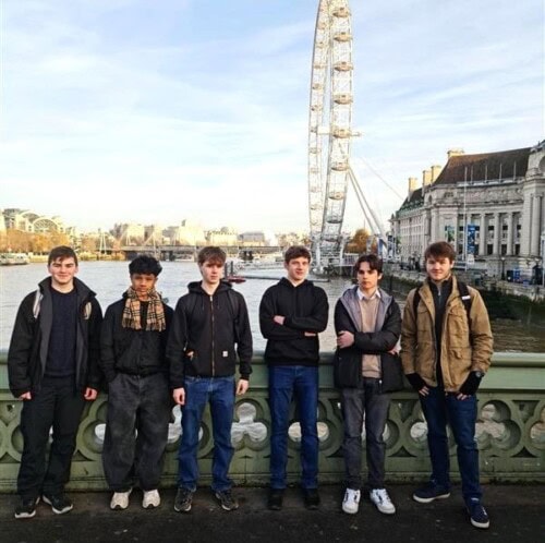 A group of male students standing on a bridge with the London eye behind them
