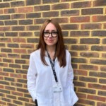 woman wearing a white shirt stands infront of a brick wall